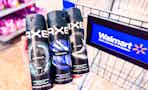 hand holding three bottles of axe body sprays in front of walmart cart in aisle