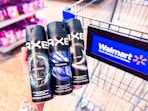 hand holding three bottles of axe body sprays in front of walmart cart in aisle
