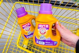 hand lifting an arm & hammer laundry detergent above a cart