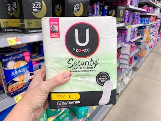 hand holding u by kotex security pads held up in front of shelves