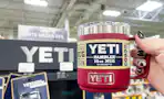 A person's hand holding a Yeti Rambler mug next to a Yeti display inside a store.