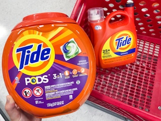 hand holding Tide pods container in front of Target shopping cart that has a Tide bottle in it