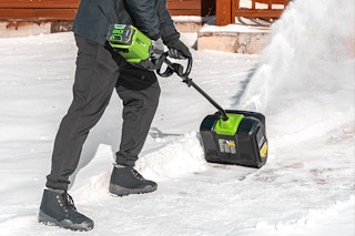 Man using the Greenworks 80V 12” Brushless Cordless Snow Shove outside on a driveway.