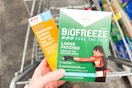 person holding biofreeze pain patches and cvs health pain relief gel over a cart