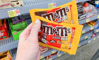 two M&M's Mix share size bags being held by left hand in front of other candy at walmart