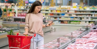 person in grocery store with cart and phone shopping for meat
