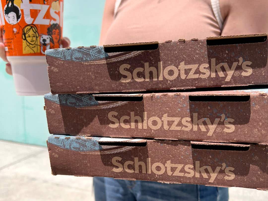 person holding three boxes and a drink from schlotzskys deli