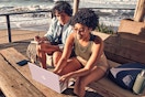 Lifestyle image of two people using a pink HP laptop outdoors near the beach