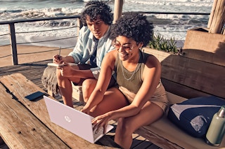Lifestyle image of two people using a pink HP laptop outdoors near the beach