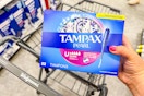 person holding a box of tampax pearl tampons over a walgreens cart