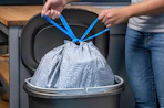 a person tying a trash bag in a trash can 