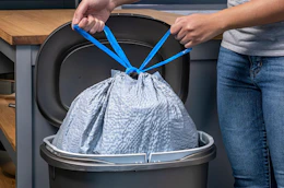 a person tying a trash bag in a trash can 