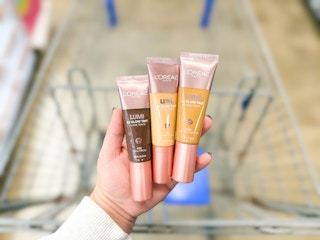 hand holding three loreal lumi foundations over walmart cart