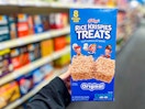 person holding a box of rice krispies treats in an aisle
