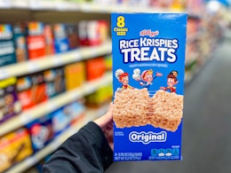 person holding a box of rice krispies treats in an aisle