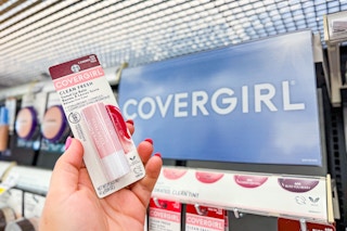person holding a covergirl lip balm by a covergirl sign