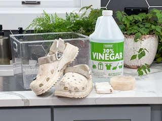 A pair of dirty Crocs on a counter next to a sink, a plastic tub, and cleaning supplies.