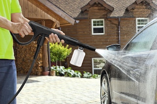 Man using a pressure power washer on his car.