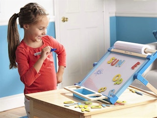 A girl smiling at her magnetic Melissa & Doug easel