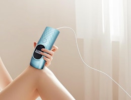 a person using a teal laser hair remover on their legs