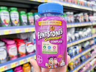 A Flintstones Gummies bottle held out in front of a store aisle.