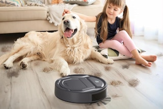 A large dog and a little girl sit on a floor that is being cleaned by the Lefant M210 robotic vacuum cleaner.