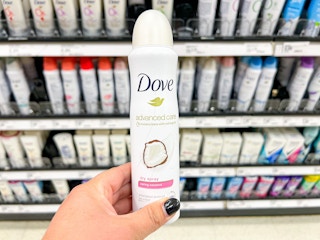 Hand holding a Dove dry spray in front of a shelf with other hygiene products
