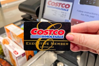 A person's hand holding up their Costco membership card in front of the self-checkout scanner at Costco.