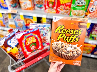 hand holding reese's puffs cereal with more cereal boxes in the background