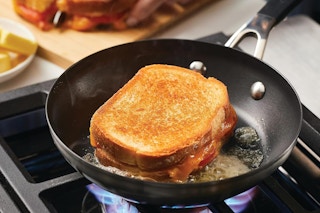 A grilled cheese sandwich cooks on a stove in a KitchenAid 8-inch frying pan.