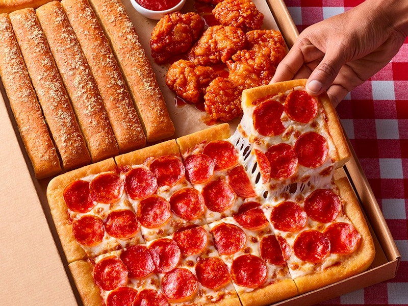 A person taking a piece of pizza from a Pizza Hut big dinner box on a table