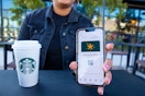 hand holding a cellphone with the starbucks app open and a cup of starbucks on a black table