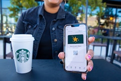 hand holding a cellphone with the starbucks app open and a cup of starbucks on a black table