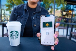 hand holding a cellphone with the starbucks app open and a cup of starbucks on a black table