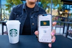 hand holding a cellphone with the starbucks app open and a cup of starbucks on a black table