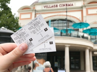 A person's hand holding two movie tickets for Mission Impossible in front of a theater showing the sales price of $5.30.