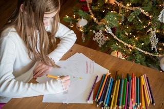 A child writing a letter at a table with colored pencils