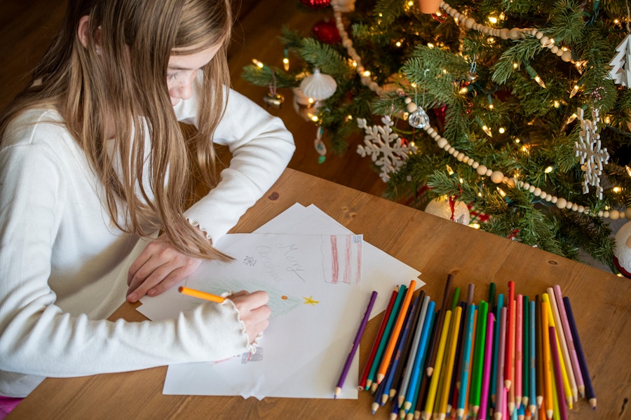 A child writing a letter at a table with colored pencils