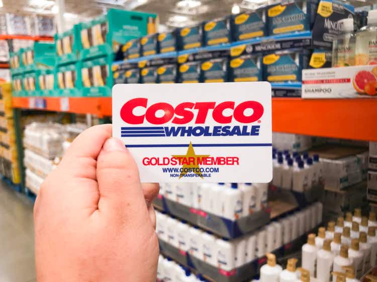 Hand holding Costco gold star member card in front of health and beauty section 
