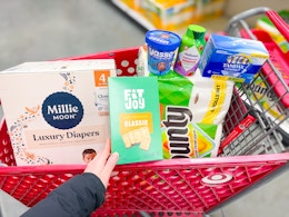 hand holding fitjoy crackers with millie moon yasso bounty vitafusion and tampax in target cart
