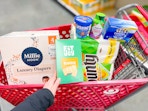 hand holding fitjoy crackers with millie moon yasso bounty vitafusion and tampax in target cart