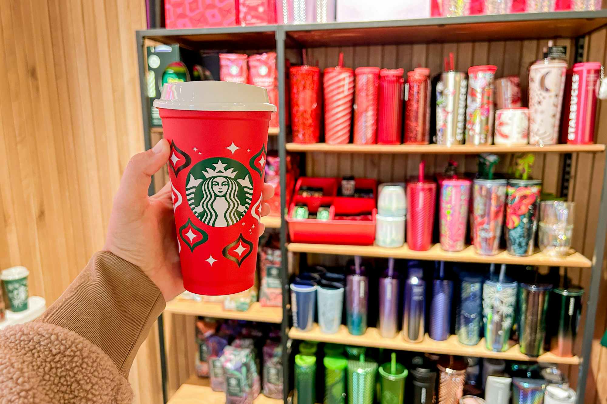 a person holding up a starbucks red cup inside of starbucks