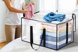 B0F4QPNZLT moving bags 6-pack - A woman's torso next to a bed with a clear moving bag on it, putting a baby outfit into the bag.