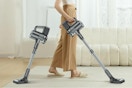the bottom half of a person using a cordless stick vacuum cleaner. Next to them is the same vacuum but shorter