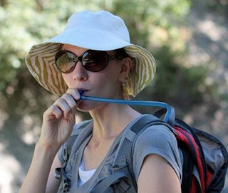 woman in a sun hat outside drinking from a hydration backpack straw
