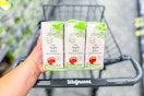 person holding a pack of apple juice boxes over a walgreens cart