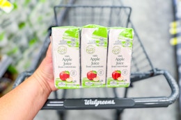 person holding a pack of apple juice boxes over a walgreens cart