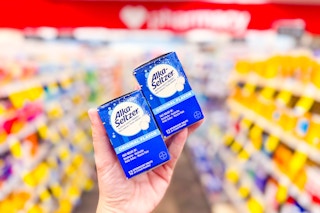person holding 2 boxes of alka seltzer tablets in an aisle