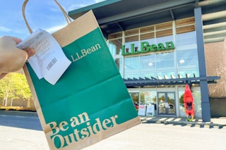 A person's hand holding up a L.L. Bean bag and receipt outside of an L.L.Bean store.