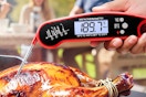 A red meat thermometer with a hole at one end and a sharp temperature taking part at the other. It also has a digital display.